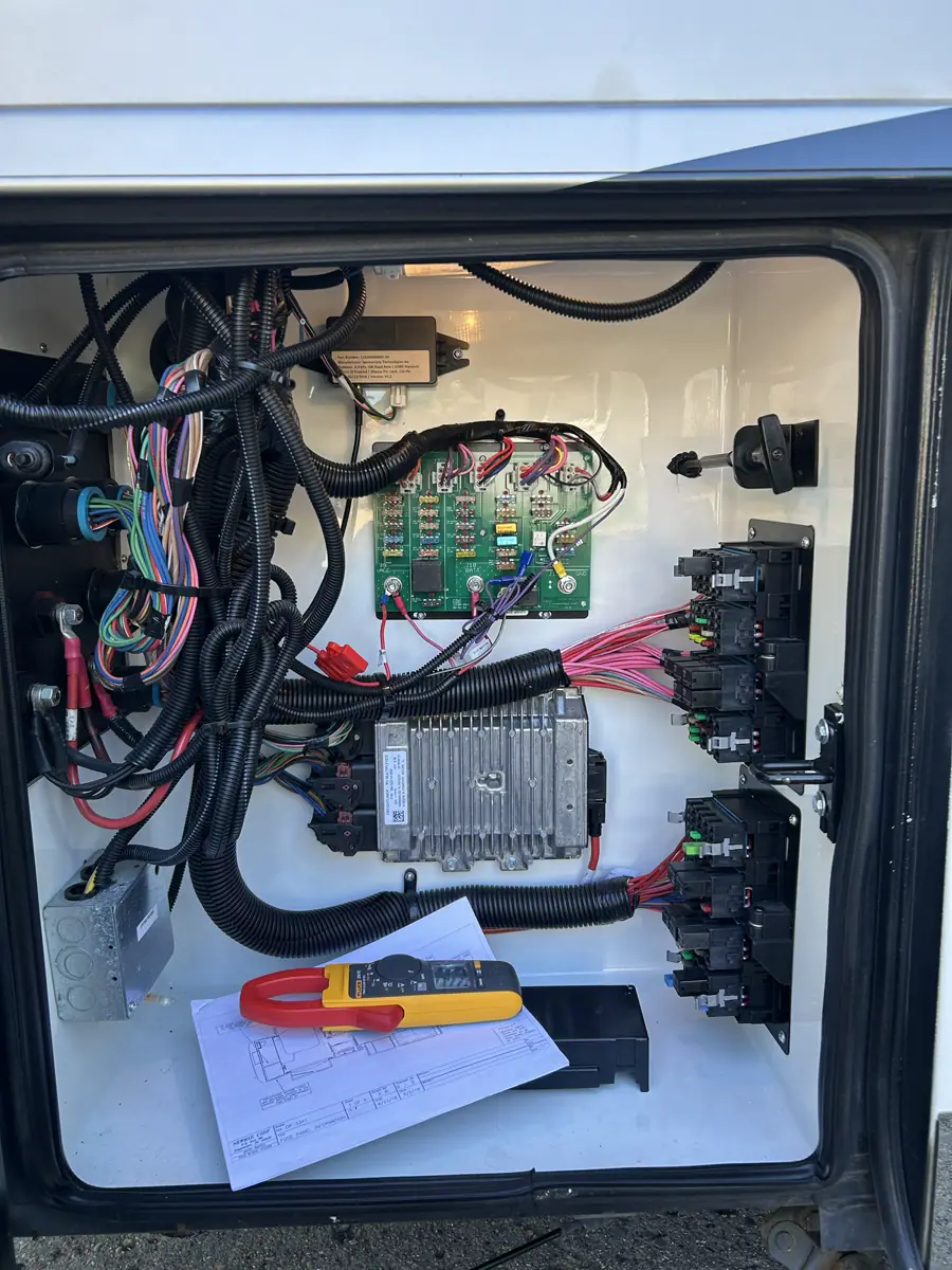Open RV electrical bay with fuse blocks and a meter on a wiring diagram during diagnostics.