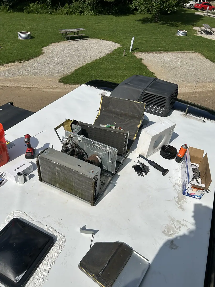 Disassembled rooftop RV air conditioner with tools and a replacement motor during a mobile roof repair.